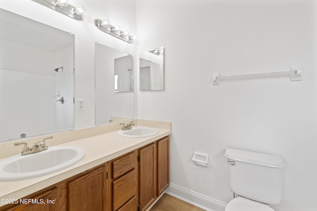 bathroom featuring toilet, a shower, double vanity, and baseboards