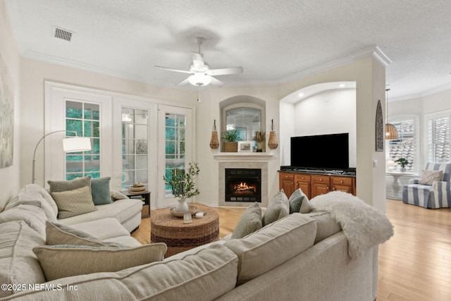 95050 Barclay Pl Unit 5B, Fernandina Beach, FL 32034 - living room featuring ceiling fan, ornamental molding, a textured ceiling, light wood-style flooring, and a lit fireplace