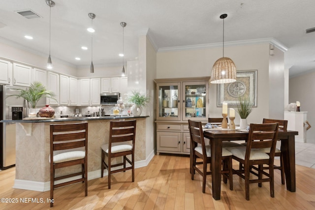 95050 Barclay Pl Unit 5B, Fernandina Beach, FL 32034 - kitchen featuring stainless steel appliances, light wood-style flooring, crown molding, a breakfast bar, and backsplash