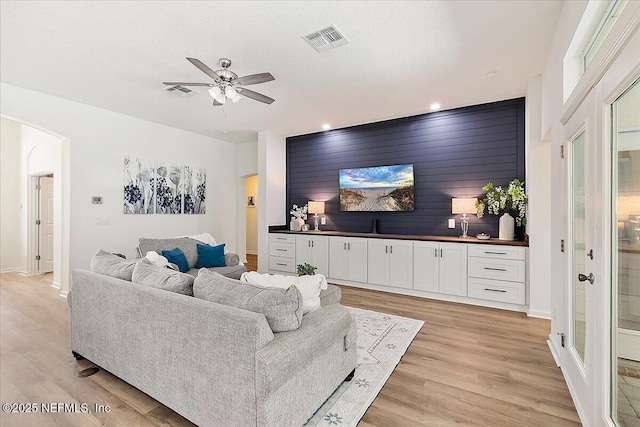 living area with a ceiling fan, light wood-type flooring, arched walkways, baseboards, and an accent wall
