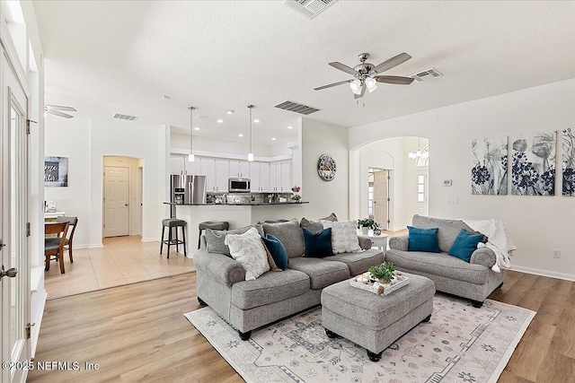living room featuring arched walkways, ceiling fan, light wood-style floors, a textured ceiling, and baseboards