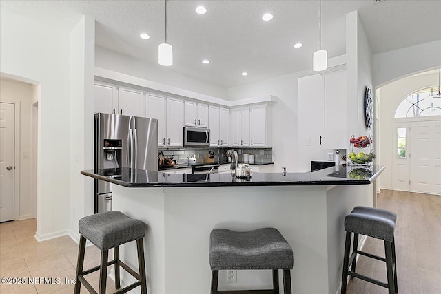 kitchen with appliances with stainless steel finishes, a breakfast bar area, decorative backsplash, dark countertops, and recessed lighting
