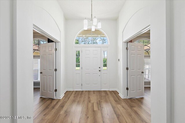 foyer entrance featuring a chandelier, light wood-style flooring, baseboards, and a textured ceiling
