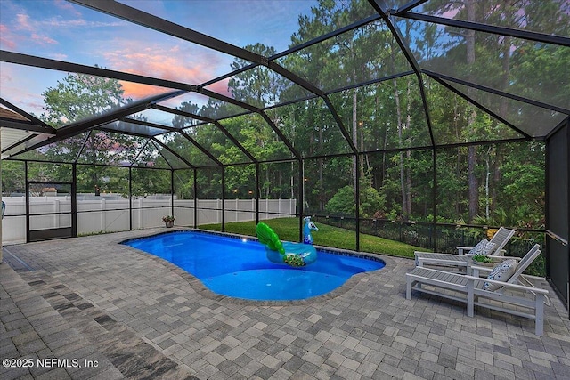 pool at dusk with a patio area, a fenced backyard, and glass enclosure