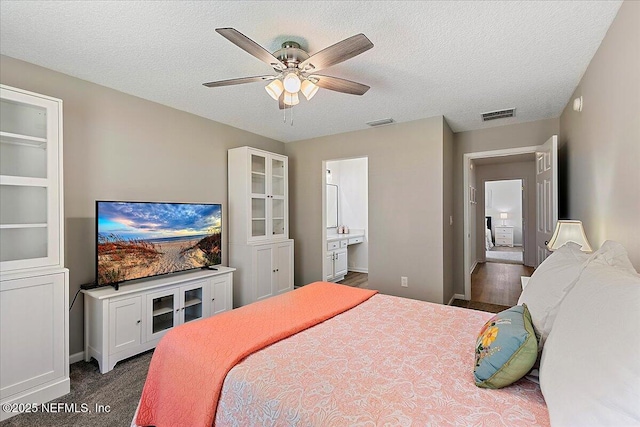 bedroom featuring a textured ceiling, ensuite bathroom, ceiling fan, baseboards, and dark carpet