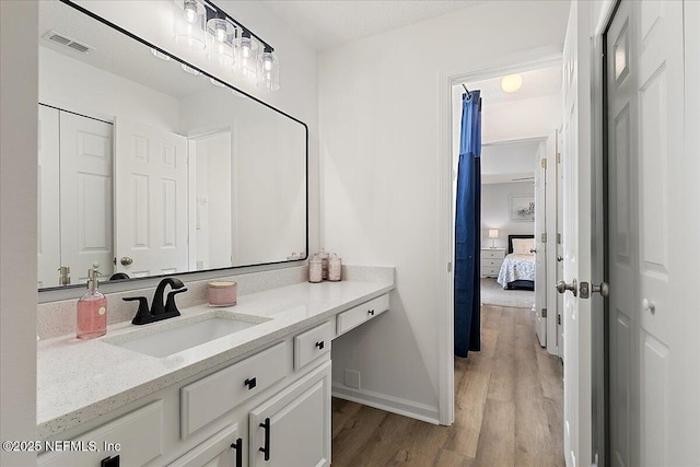 ensuite bathroom with wood finished floors, vanity, and baseboards