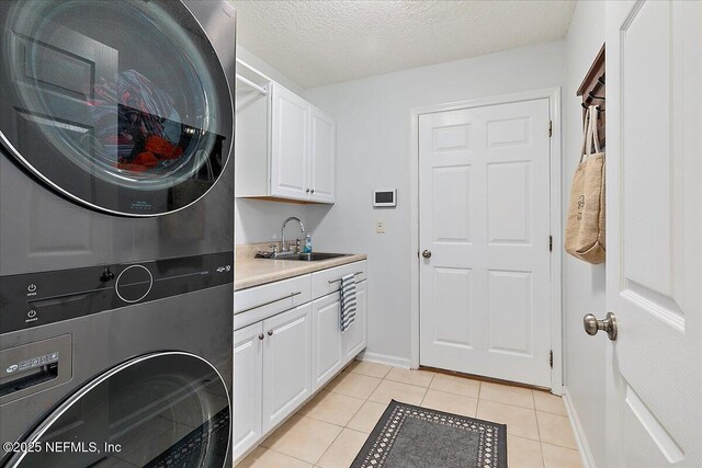 laundry area featuring stacked washer / dryer, cabinet space, light tile patterned floors, baseboards, and a textured ceiling
