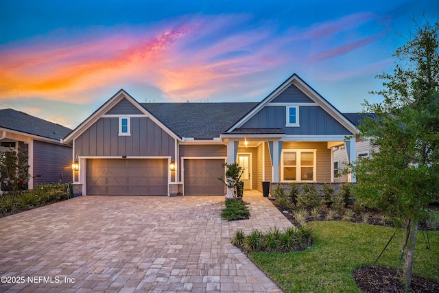 craftsman-style home with board and batten siding, decorative driveway, an attached garage, and a yard