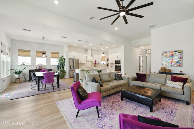 living room featuring light wood finished floors, ceiling fan, recessed lighting, a chandelier, and baseboards