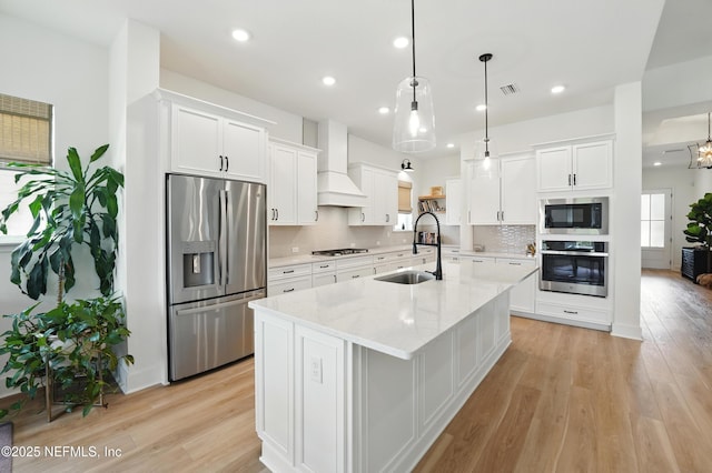 kitchen featuring stainless steel appliances, premium range hood, white cabinetry, light wood-style floors, and tasteful backsplash