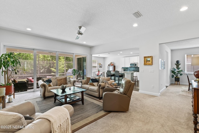 living area featuring light carpet, a textured ceiling, recessed lighting, baseboards, and a ceiling fan