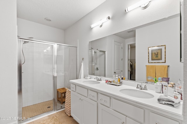 full bath featuring a shower stall, double vanity, and a textured ceiling