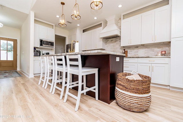 4282 Wolfe Dr, Macclenny, FL 32063 - kitchen with premium range hood, stainless steel microwave, backsplash, light wood-type flooring, and a breakfast bar