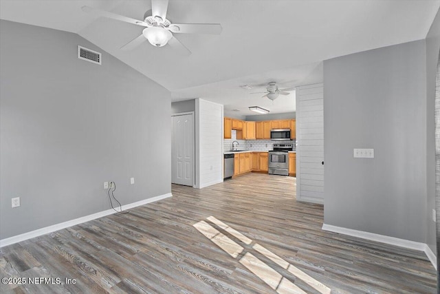 unfurnished living room featuring ceiling fan, light wood-style floors, a sink, baseboards, and vaulted ceiling