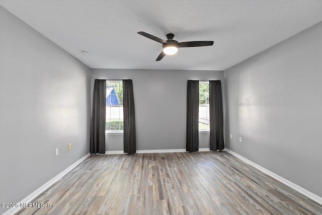 spare room featuring wood finished floors, plenty of natural light, a ceiling fan, a textured ceiling, and baseboards