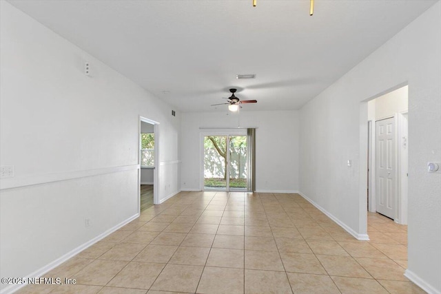 empty room with ceiling fan, light tile patterned floors, and baseboards