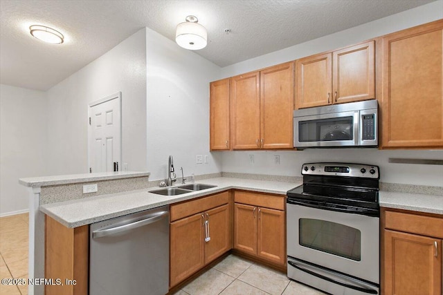 kitchen with appliances with stainless steel finishes, a sink, light tile patterned flooring, a peninsula, and a textured ceiling