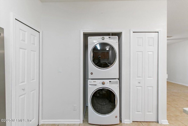 laundry room with estacked washer and dryer, light tile patterned flooring, and baseboards