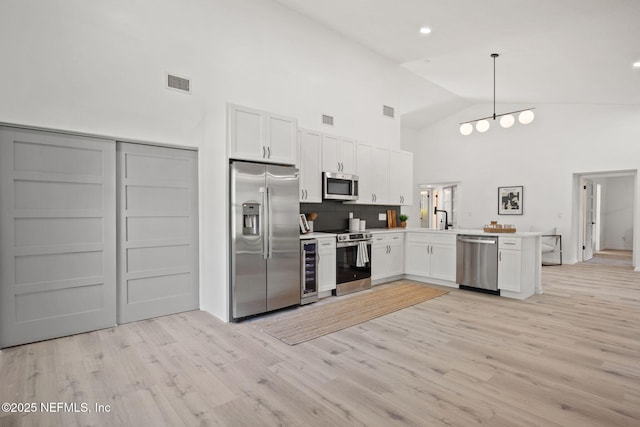 550 Robles Ln, Ponte Vedra Beach, FL 32082 - kitchen featuring appliances with stainless steel finishes, a peninsula, high vaulted ceiling, light wood-style floors, and white cabinets