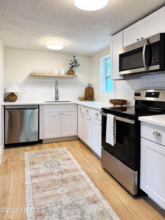 kitchen featuring appliances with stainless steel finishes, a sink, light countertops, decorative backsplash, and light wood-type flooring