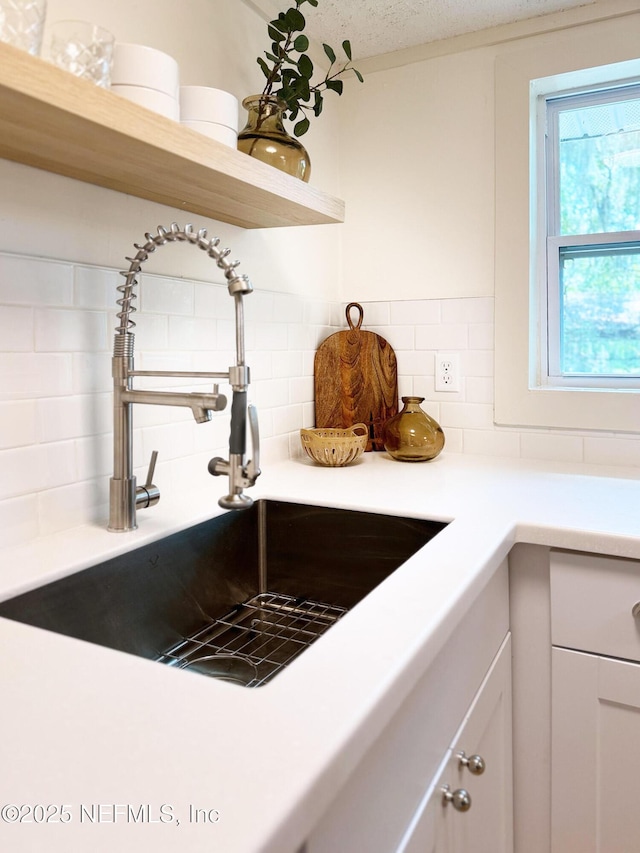 kitchen view of a sink, tasteful backsplash, light countertops, white cabinets, and open shelves