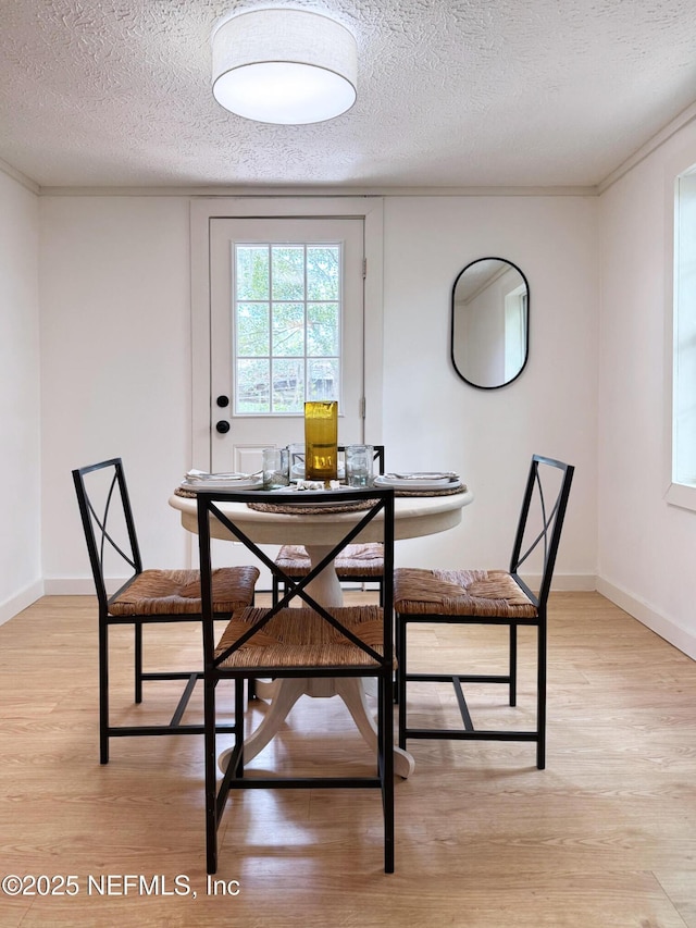 dining room featuring light wood-style floors, a textured ceiling, and baseboards