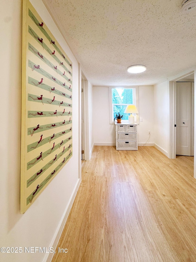 hallway with wood finished floors, a textured ceiling, and baseboards