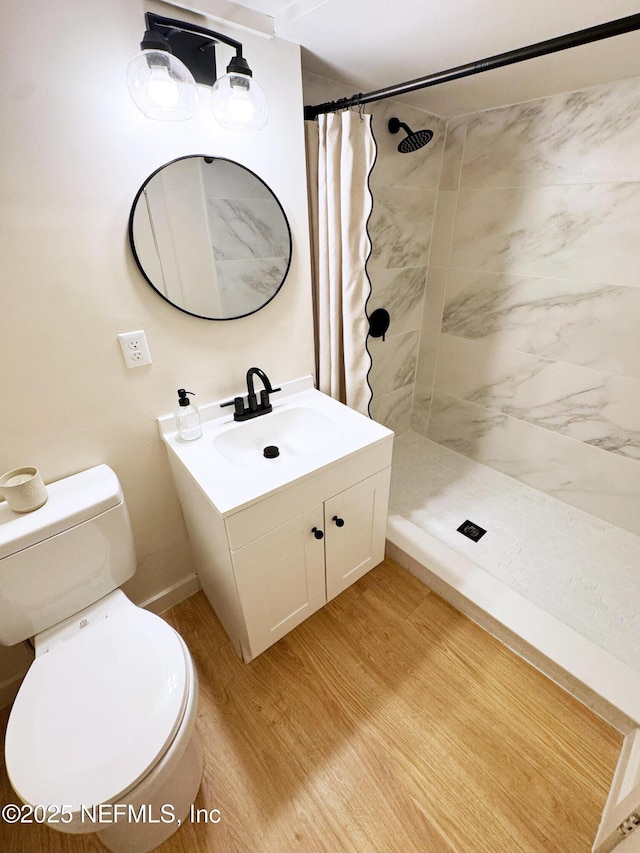 full bathroom with toilet, tiled shower, vanity, and wood finished floors