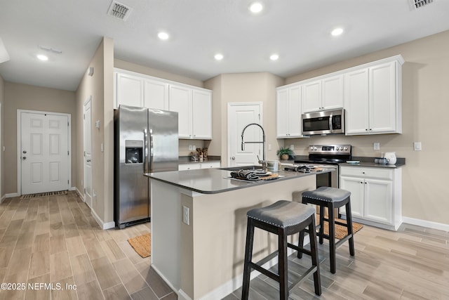 kitchen with stainless steel appliances, a sink, baseboards, light wood finished floors, and white cabinetry