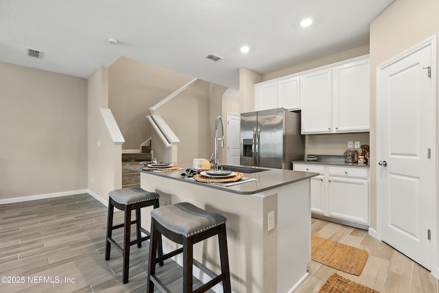 kitchen featuring stainless steel fridge with ice dispenser, light wood-type flooring, a breakfast bar, white cabinets, and recessed lighting