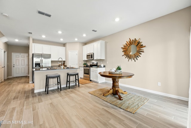 kitchen with appliances with stainless steel finishes, a breakfast bar, baseboards, light wood-style floors, and recessed lighting