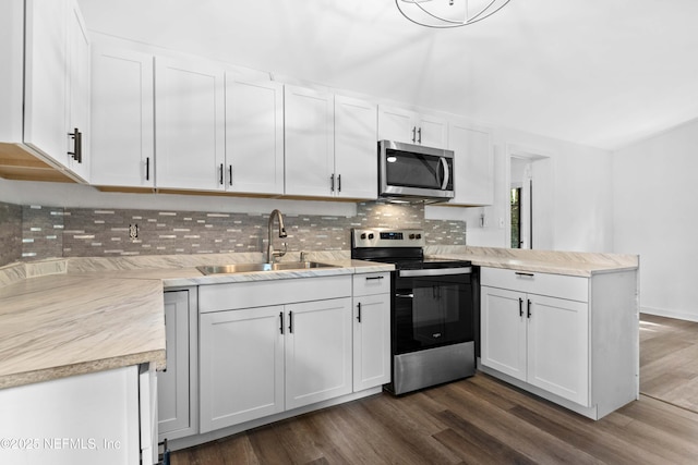 kitchen featuring stainless steel appliances, a sink, a peninsula, backsplash, and white cabinetry