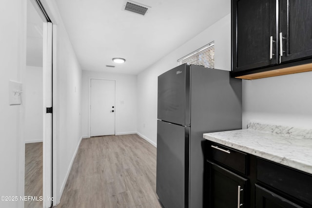 kitchen with dark cabinetry, freestanding refrigerator, light wood-style floors, and baseboards