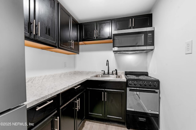 kitchen with stainless steel appliances, a sink, dark cabinets, and light stone counters