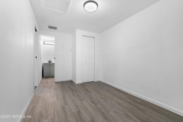 unfurnished bedroom with wood finished floors, baseboards, a closet, and attic access