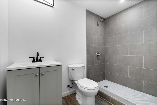 bathroom with a tile shower, toilet, wood finished floors, vanity, and baseboards