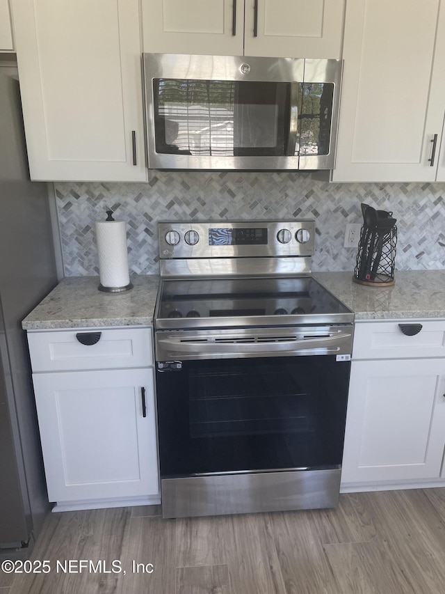 kitchen with stainless steel appliances, white cabinetry, and backsplash