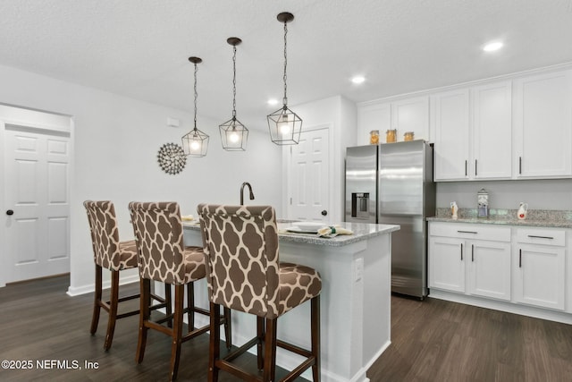 kitchen with stainless steel refrigerator with ice dispenser, dark wood-style floors, a breakfast bar area, white cabinetry, and recessed lighting