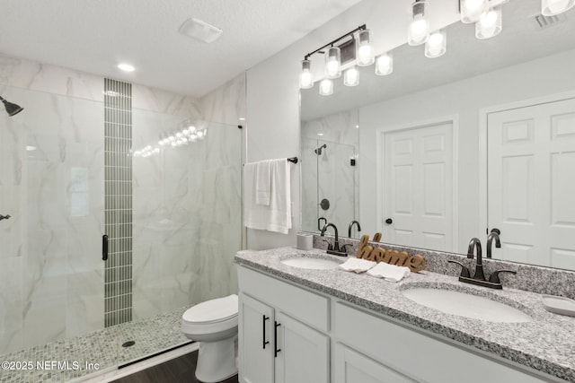 bathroom with toilet, a marble finish shower, and double vanity