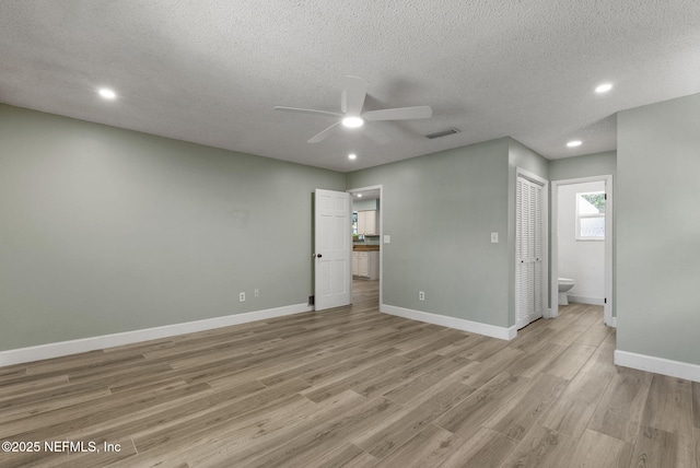 unfurnished bedroom featuring light wood-style floors, recessed lighting, a textured ceiling, baseboards, and ensuite bath