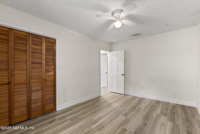 unfurnished bedroom featuring a closet, light wood-style floors, a textured ceiling, and baseboards