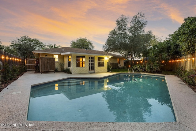 pool at dusk with a fenced backyard and a patio