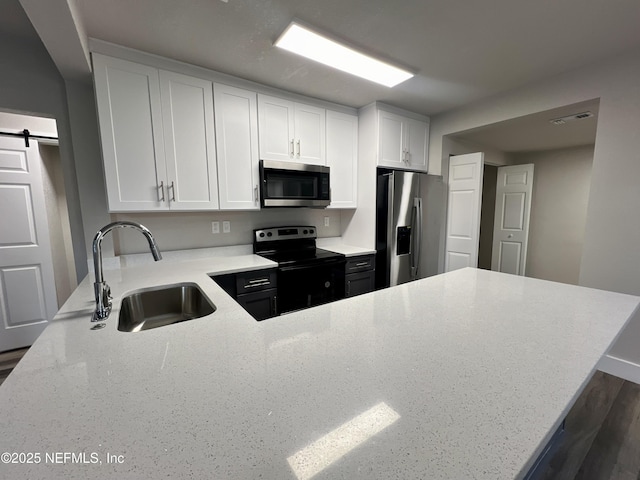3133 Gilmore St, Jacksonville, FL 32205 - kitchen with stainless steel appliances, a sink, light stone countertops, white cabinetry, and a barn door
