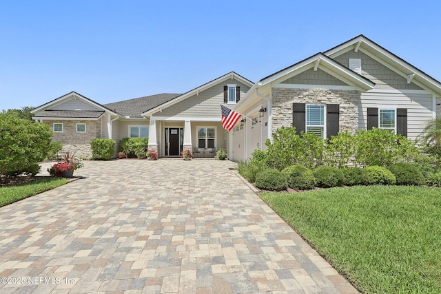 craftsman house with stone siding, decorative driveway, a garage, and a front lawn