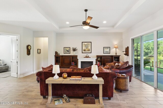 living area with a raised ceiling, a ceiling fan, a fireplace, light wood-type flooring, and recessed lighting