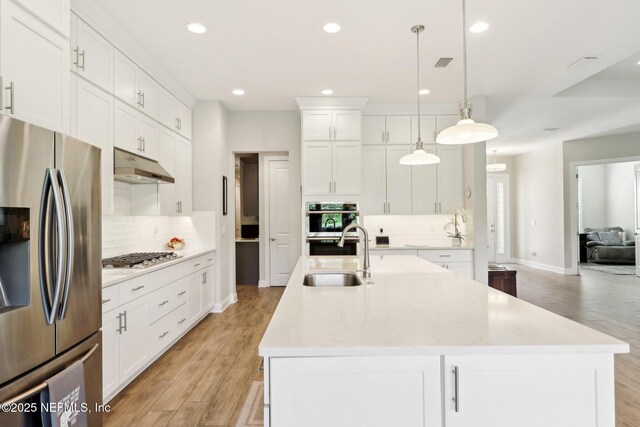 kitchen with stainless steel appliances, under cabinet range hood, a sink, decorative backsplash, and light countertops