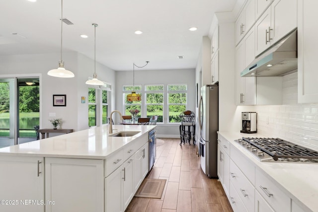 kitchen featuring a sink, appliances with stainless steel finishes, under cabinet range hood, a center island with sink, and tasteful backsplash