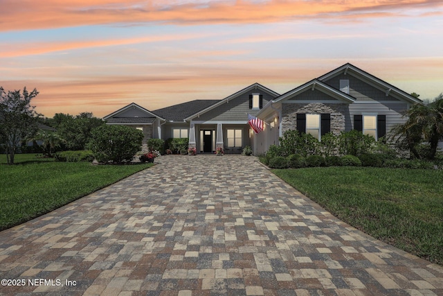 craftsman house with decorative driveway, a front lawn, and stone siding