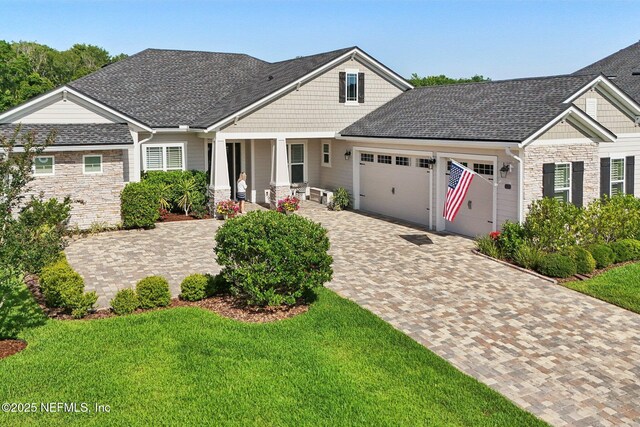 craftsman inspired home featuring stone siding, a garage, covered porch, a front yard, and decorative driveway