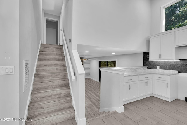 2032 Sandpiper Pt, Neptune Beach, FL 32266 - kitchen featuring white cabinets, a high ceiling, tasteful backsplash, light wood-type flooring, and a peninsula